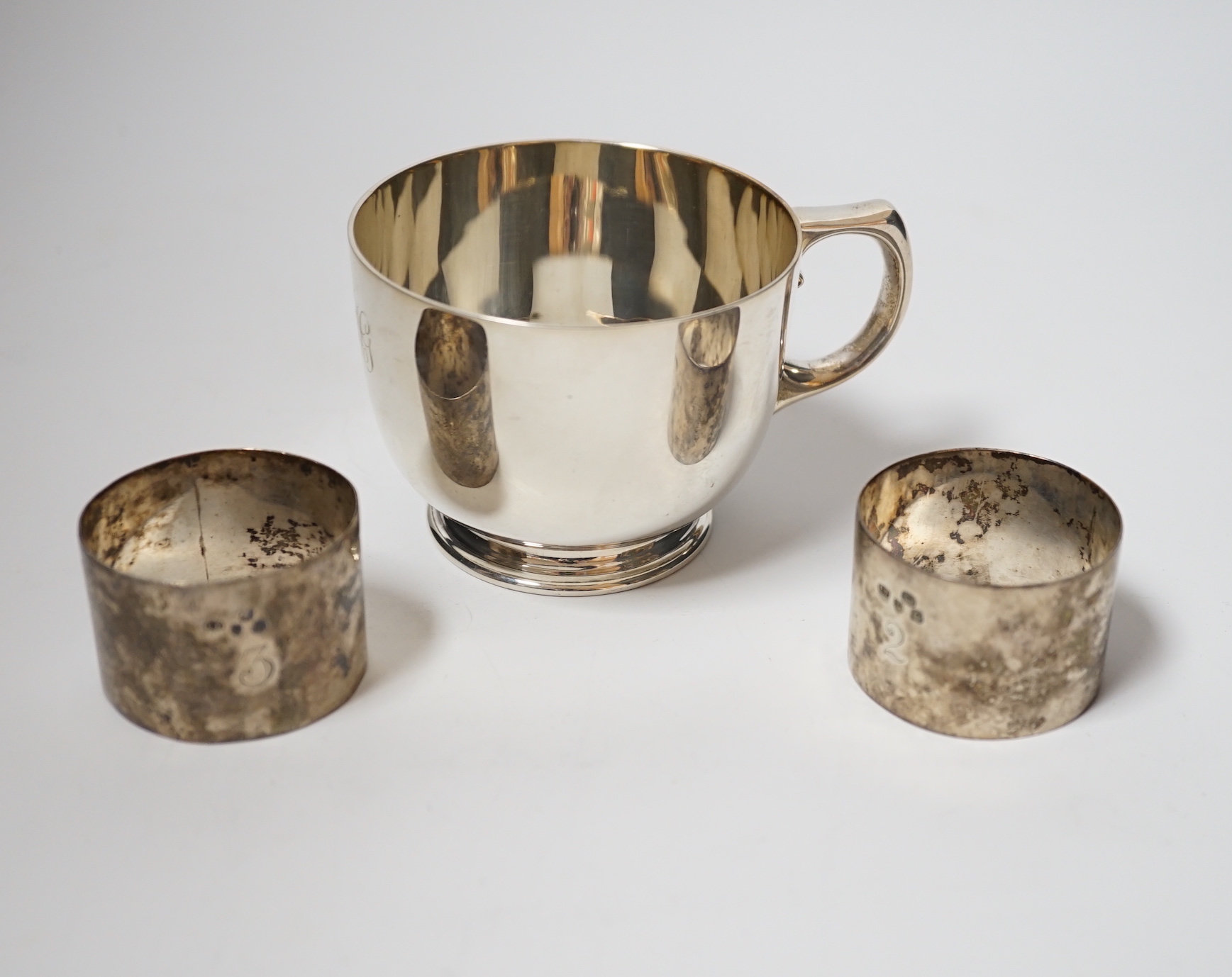 A George V silver cup, with single handle, Searle & Co, London, 1932, height 61mm, together with a pair of late Victorian silver napkin rings, Charles Edwards, London, 1899, 8oz.